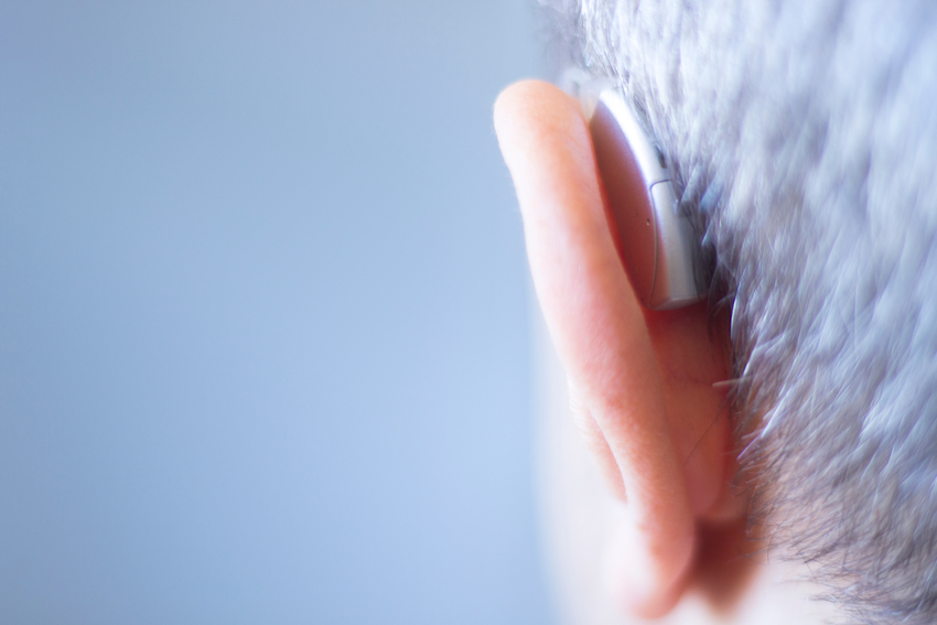 A detail photograph of the back of an older mans head. He's wearing a hearing aid and you can see the hearing aid wrapping around the back of th ear. 