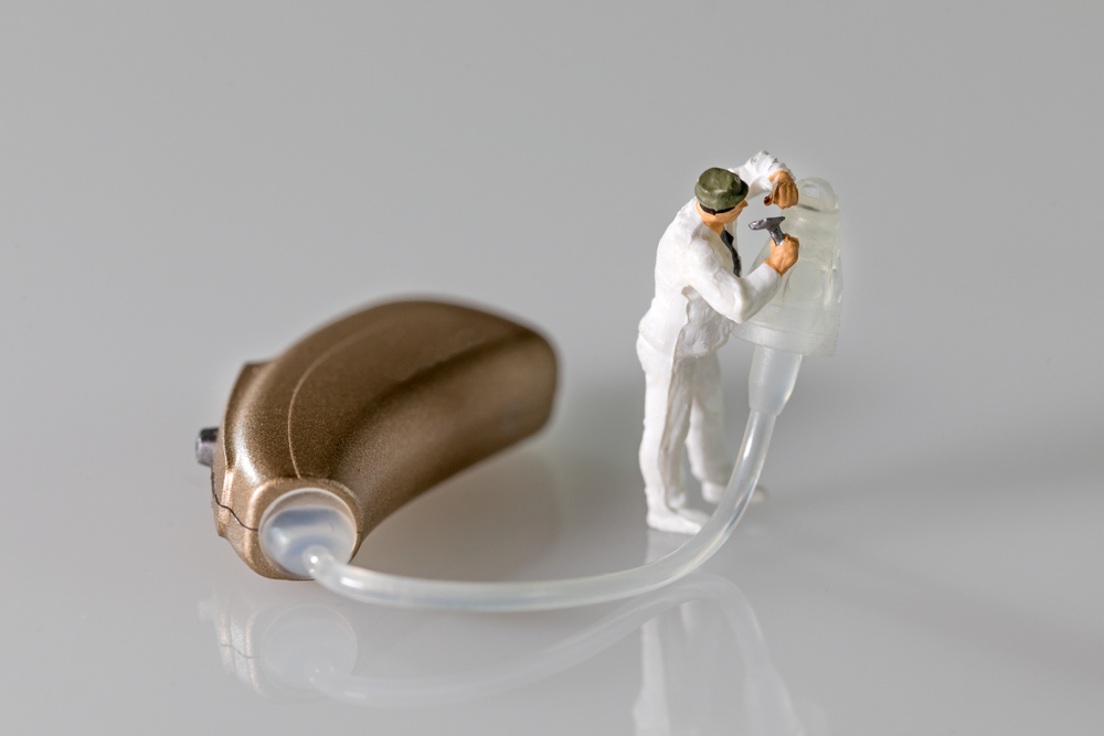 Hearing aid with a small figurine attempting to fix it.